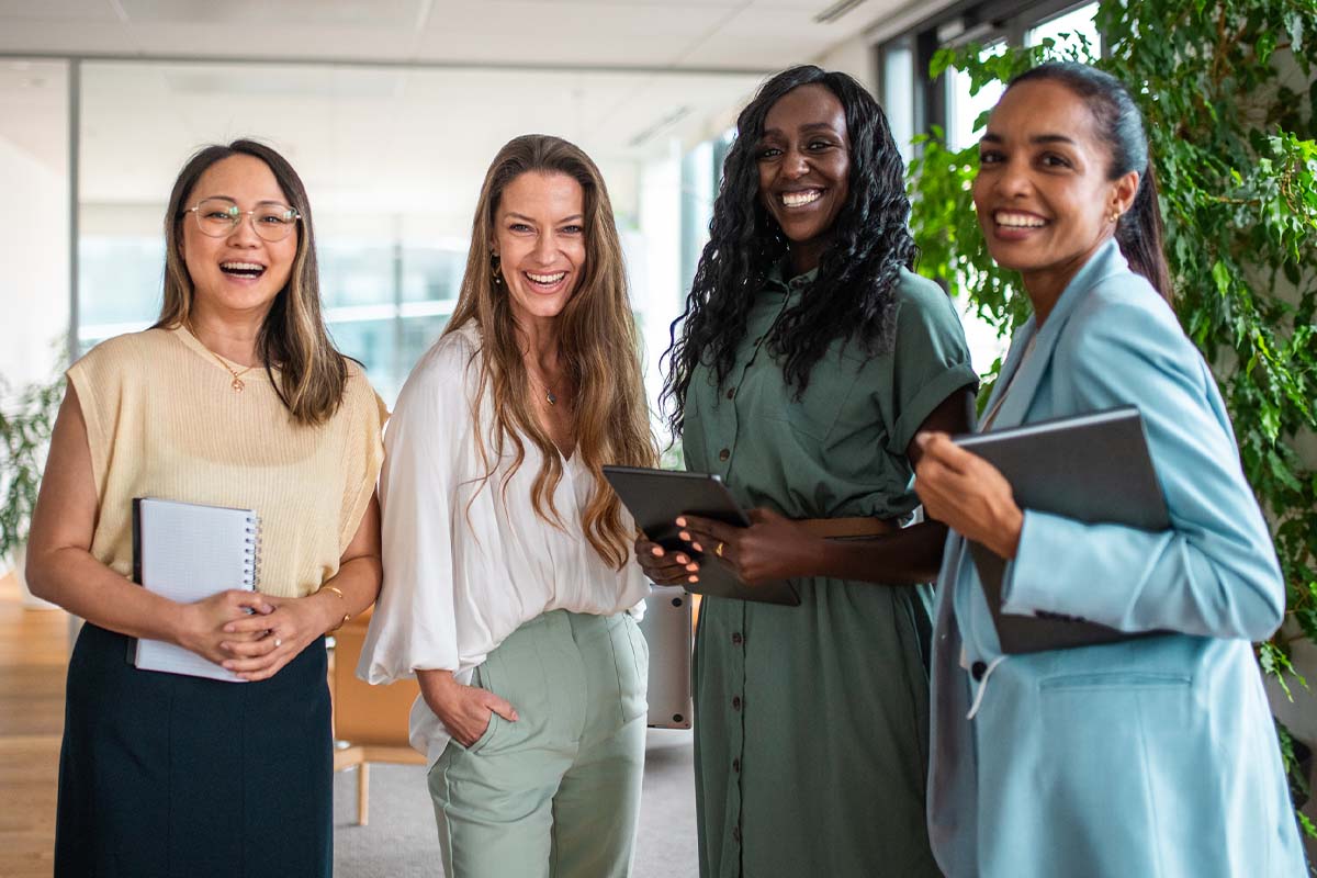 four women standing together and smiling while holding tablets at an office after getting vaginal rejuvenation in McAllen.